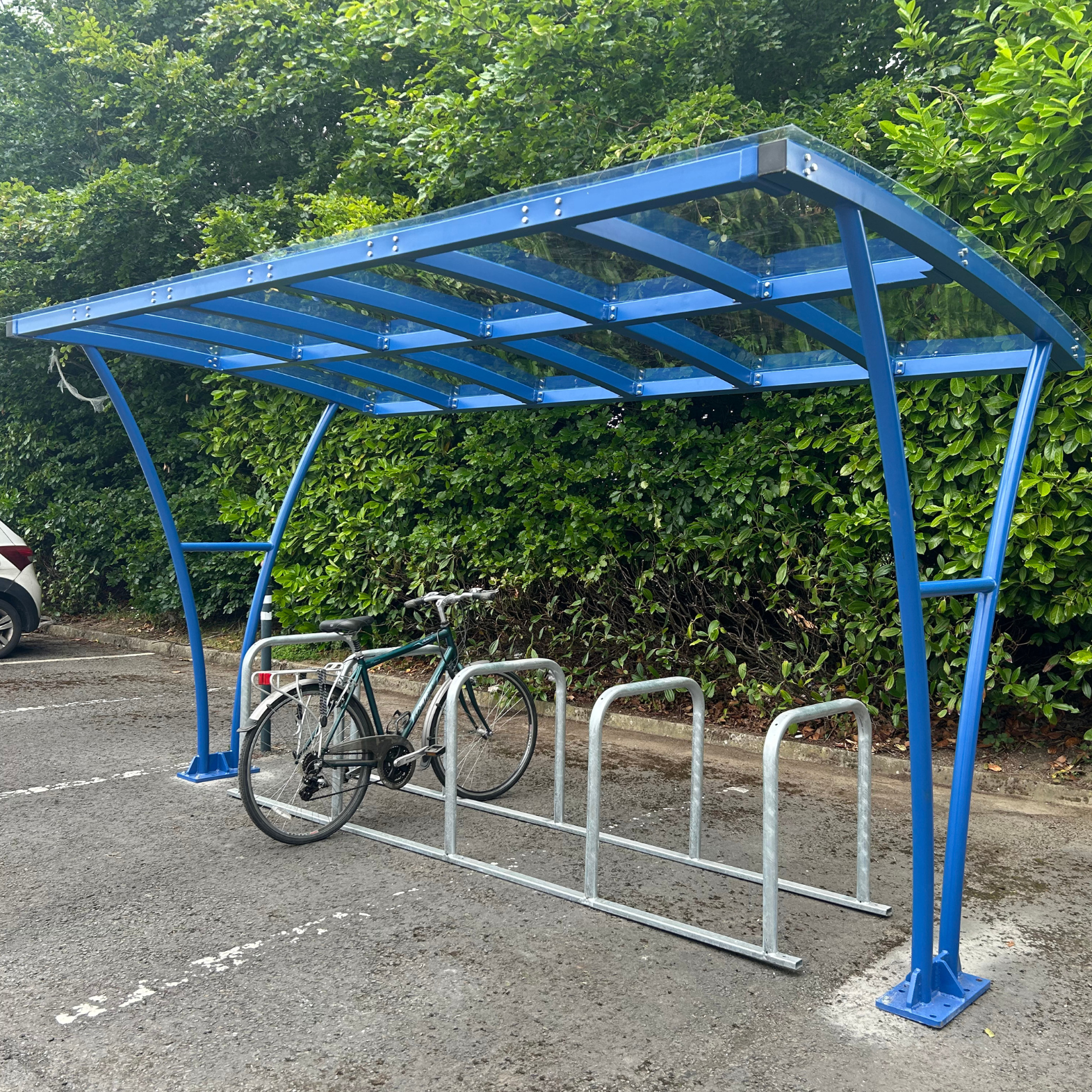 Blue bicycle shelter with a bike parked underneath in a parking lot.