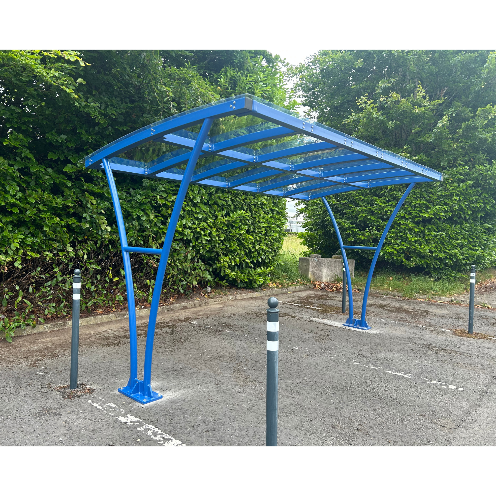 Blue metal carport structure on a driveway with greenery in the background
