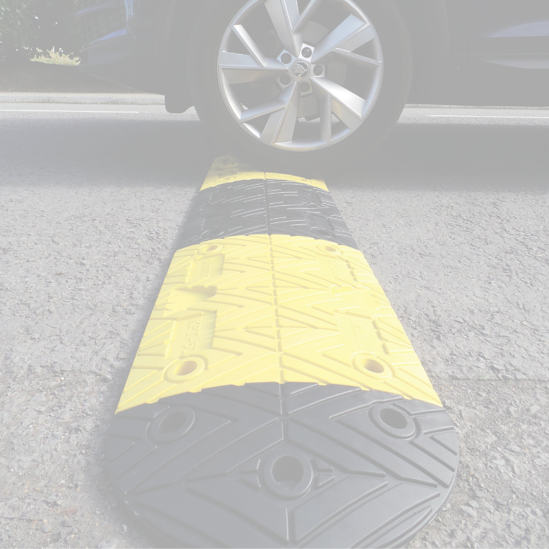 Car approaching a yellow and black speed bump on a road.