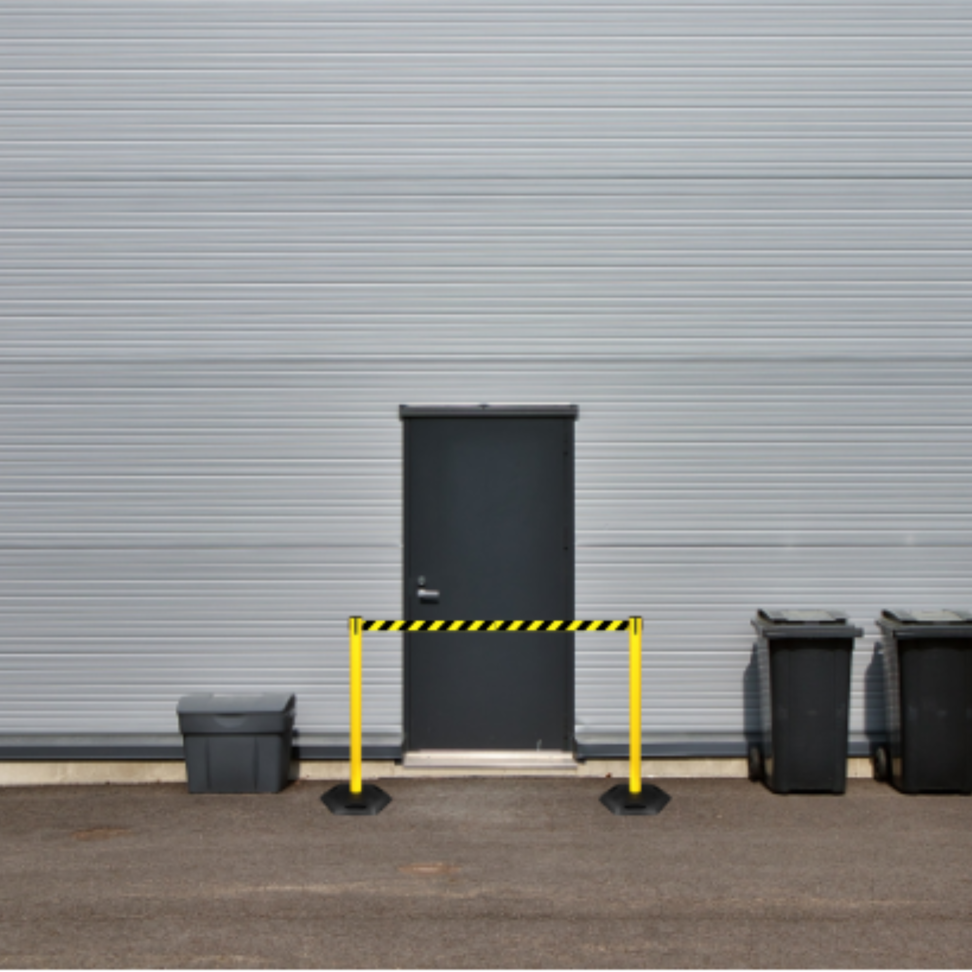 Black trash bins with yellow caution tape against a gray industrial building.