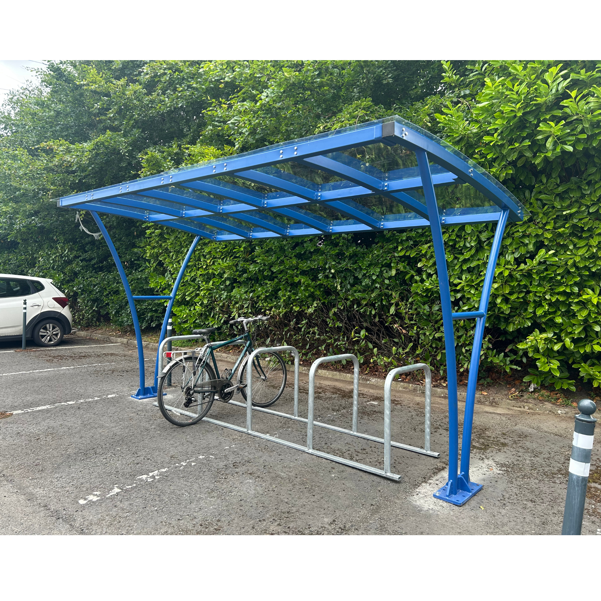Blue bicycle shelter with a bike parked underneath in a parking lot.