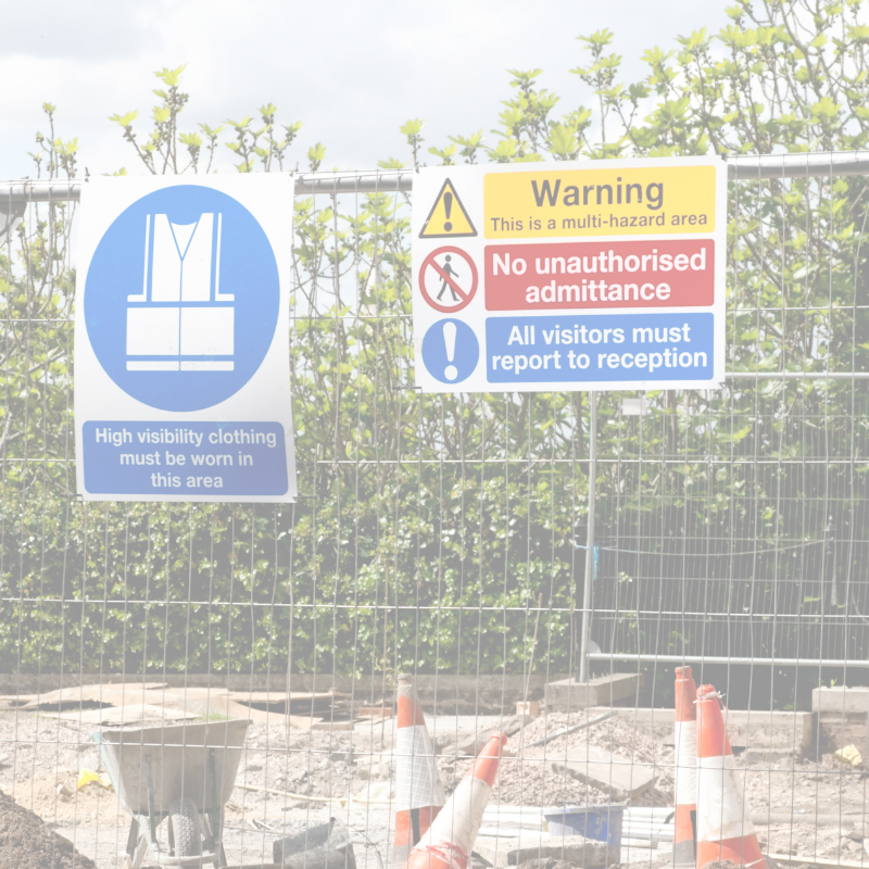 Safety signs on a fence with construction cones and equipment in the foreground.